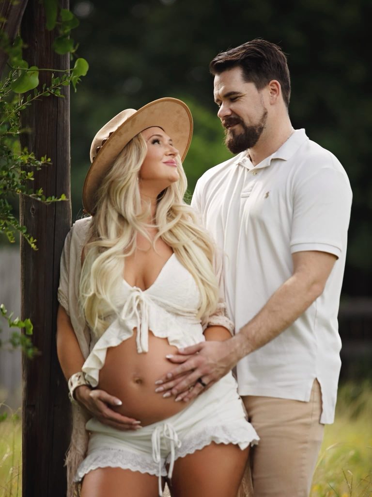 An expectant couple outdoors with long blonde waves and soft makeup
